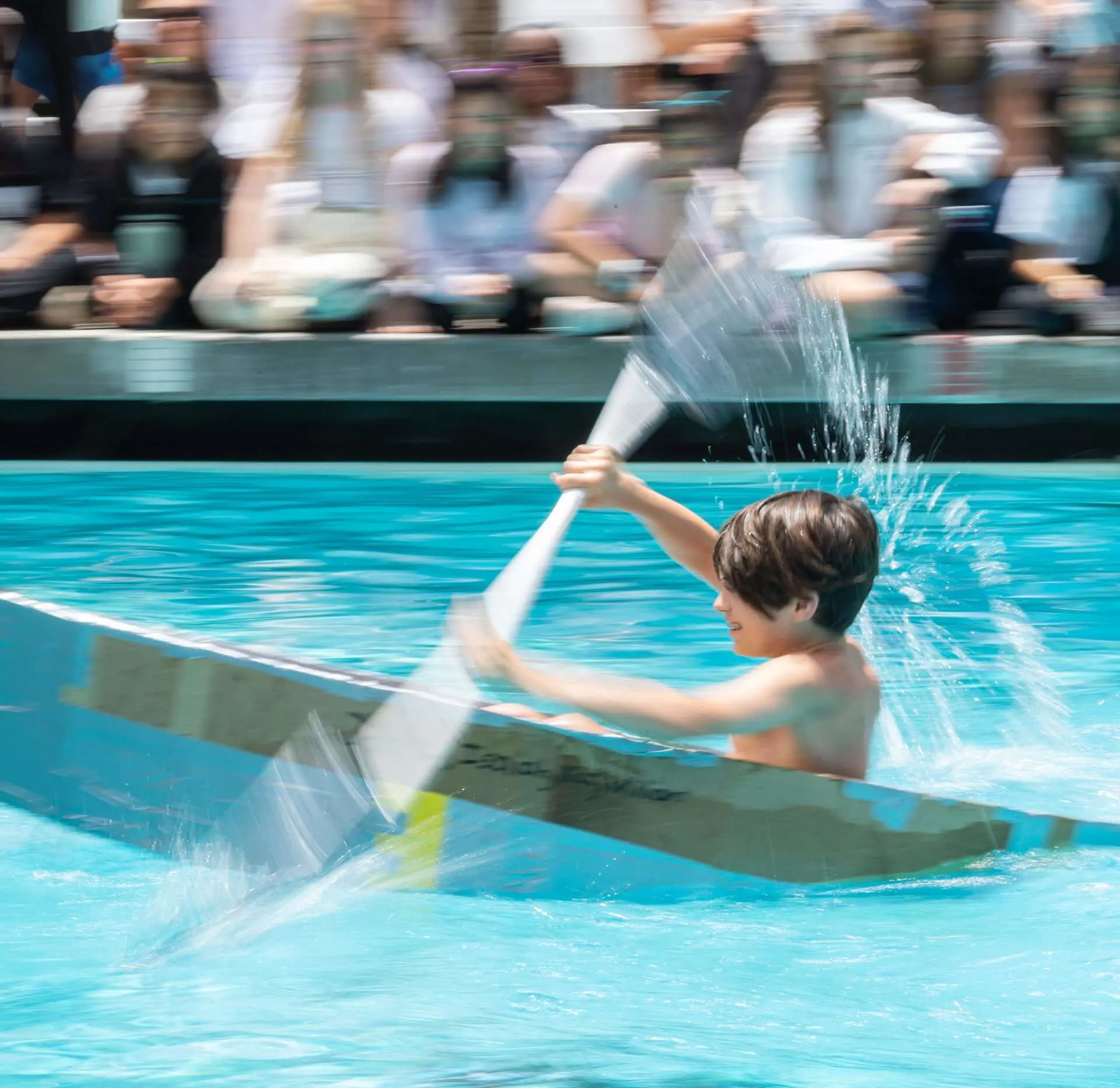 A camper paddles a cardboard boat during boat races.