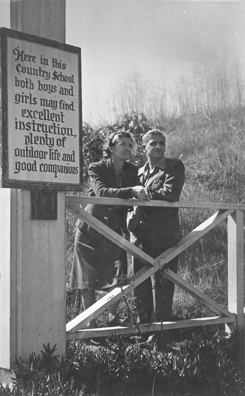 Founder Margaret Chadwick stands next to a sign that reads, “Here in this Country School, both boys and girls may find excellent instruction, plenty of outdoor life and good companions.”