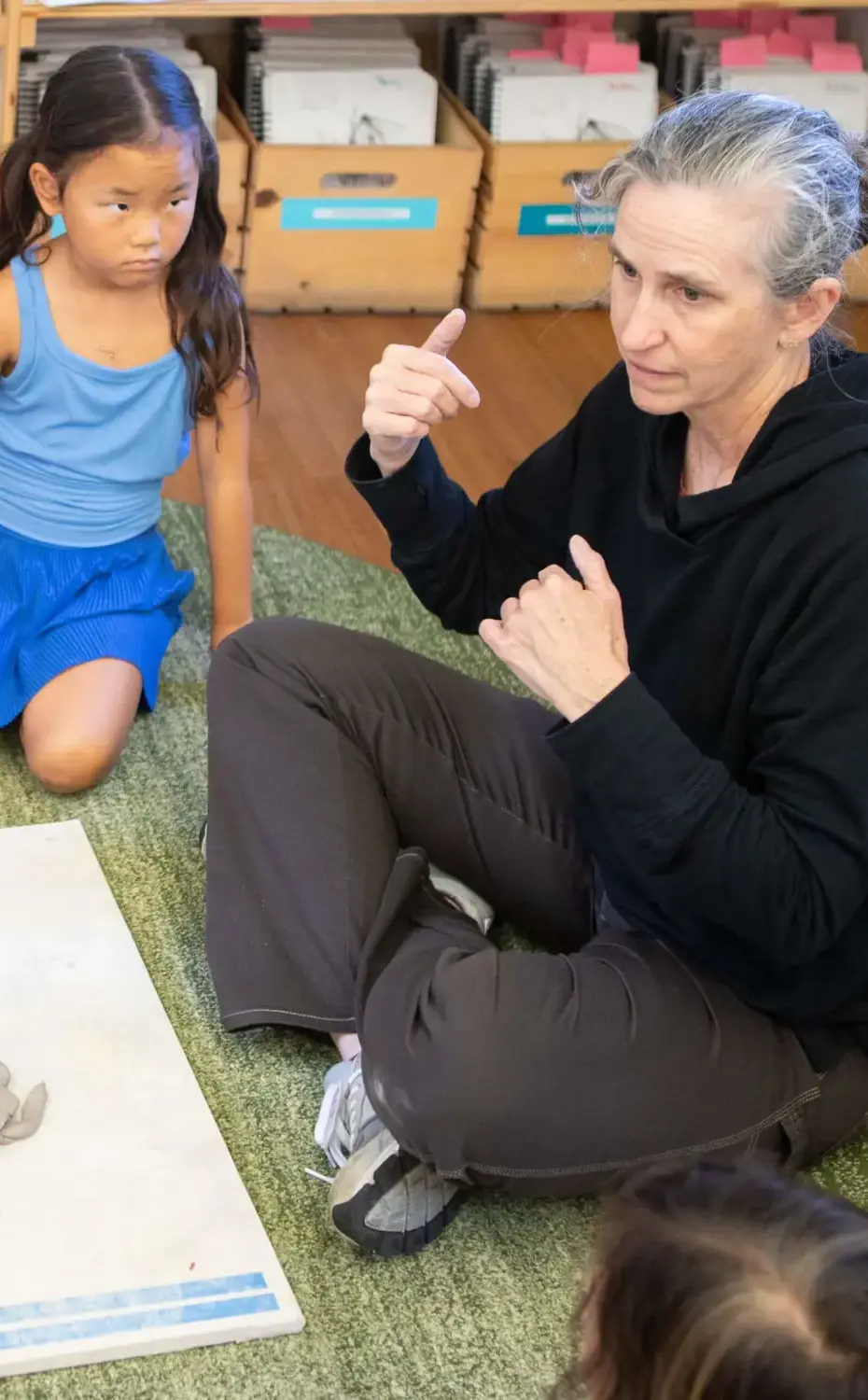 Village art teachers talks about ceramic with students as they sit in a circle.