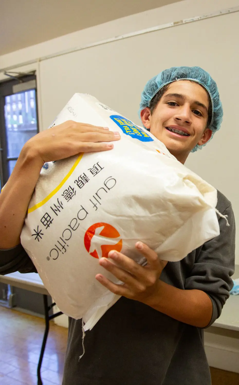 8th Grade student carries a bag of rice at the Middle School day of service.