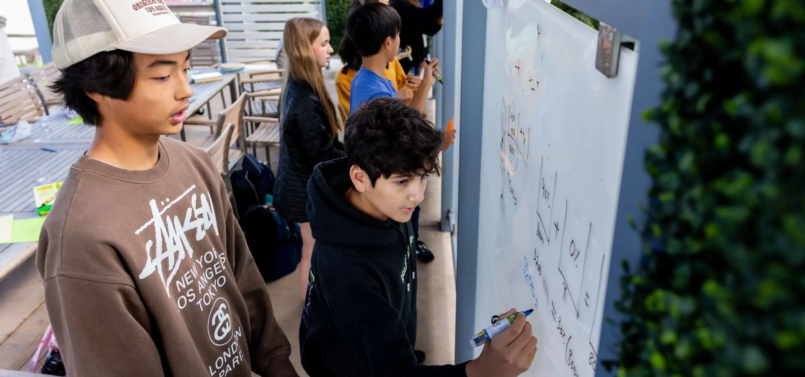 Middle School students work together on a math problem on the whiteboard outside in the Outdoor Living and Learning Space.