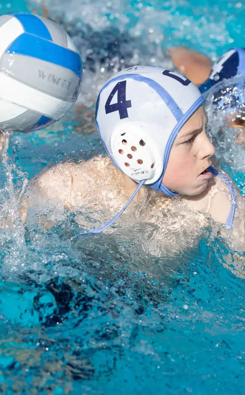 Chadwick sixth grader raises ball white water splashes around them during a water polo match.