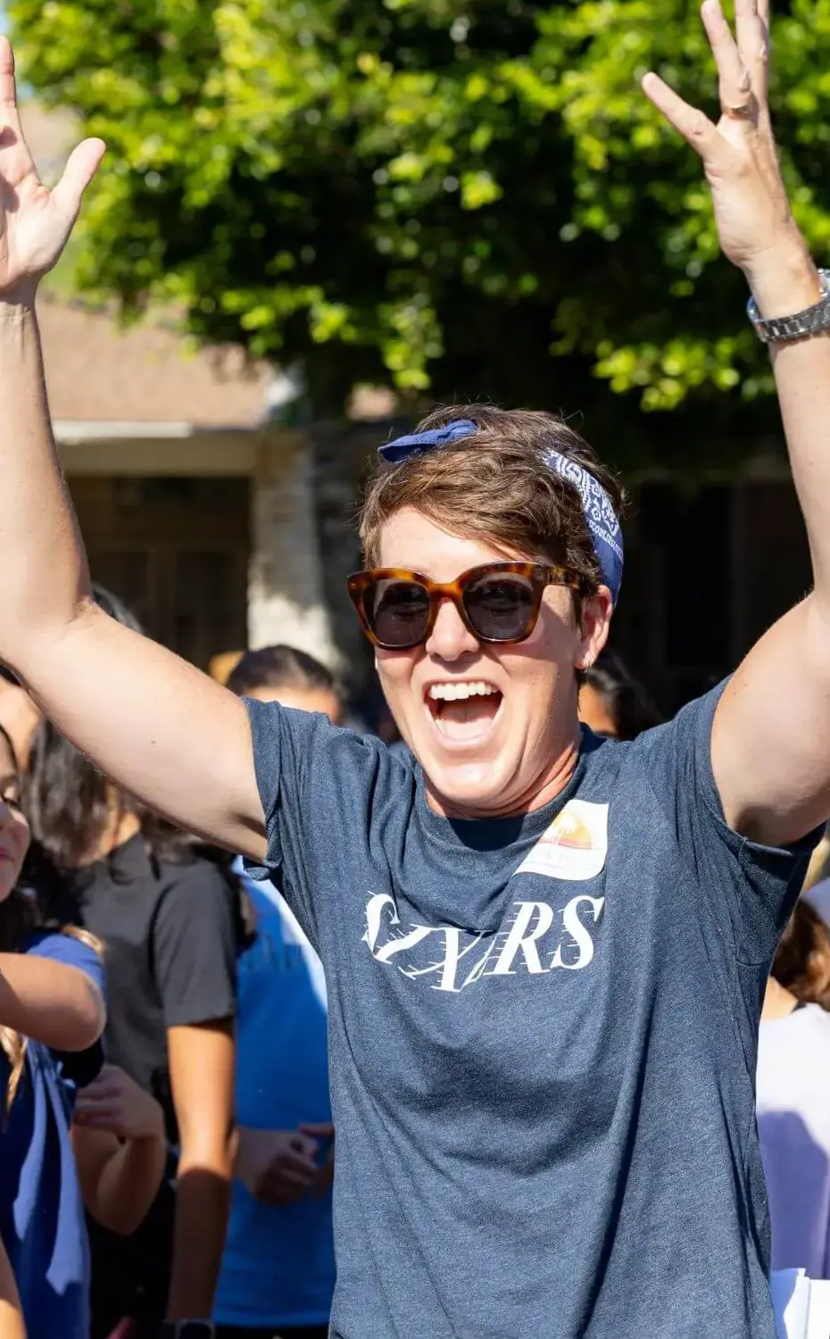 Sixth-grade teacher celebrates with their arms in the air, surrounded by students.