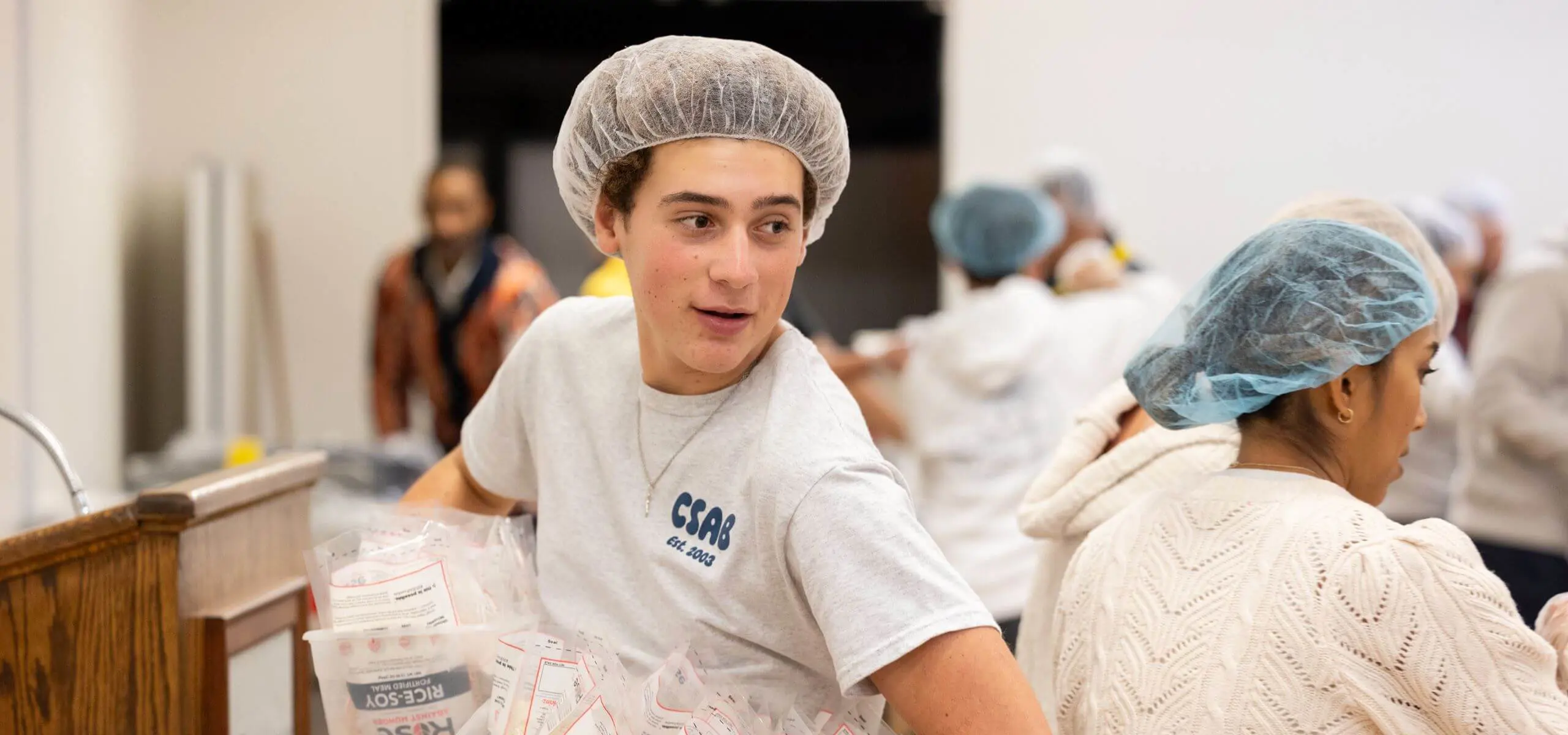 Student in a hairnet holds packaged food during the Hung Banquet meal packing event.