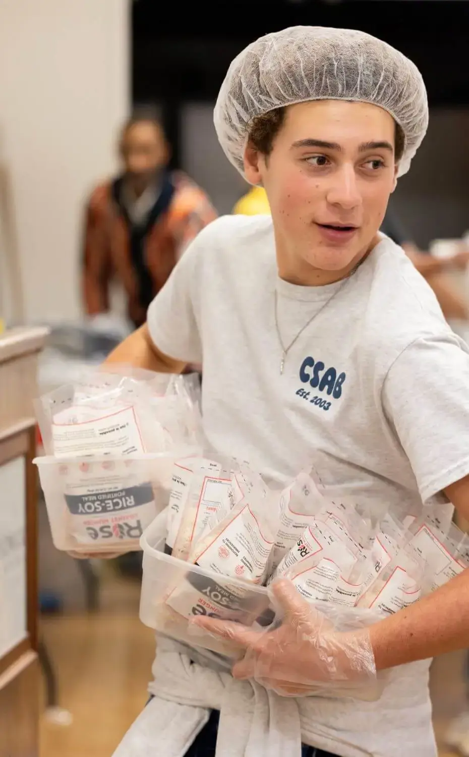 Student in a hairnet holds packaged food during the Hung Banquet meal packing event.