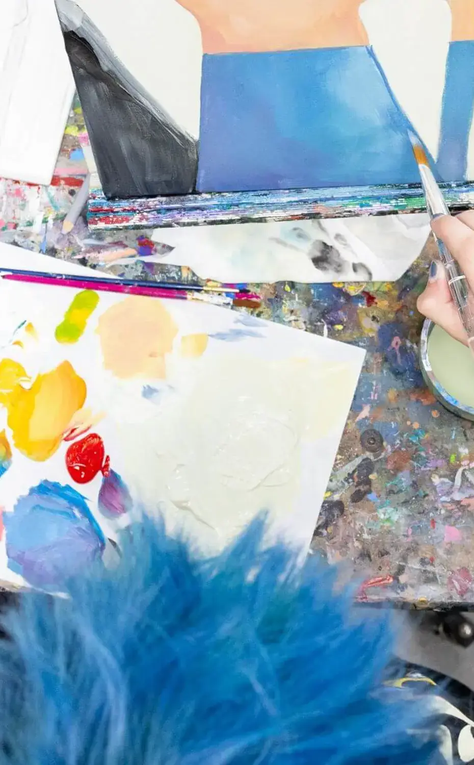Student with blue hair works on painting of still life in a top down photo.