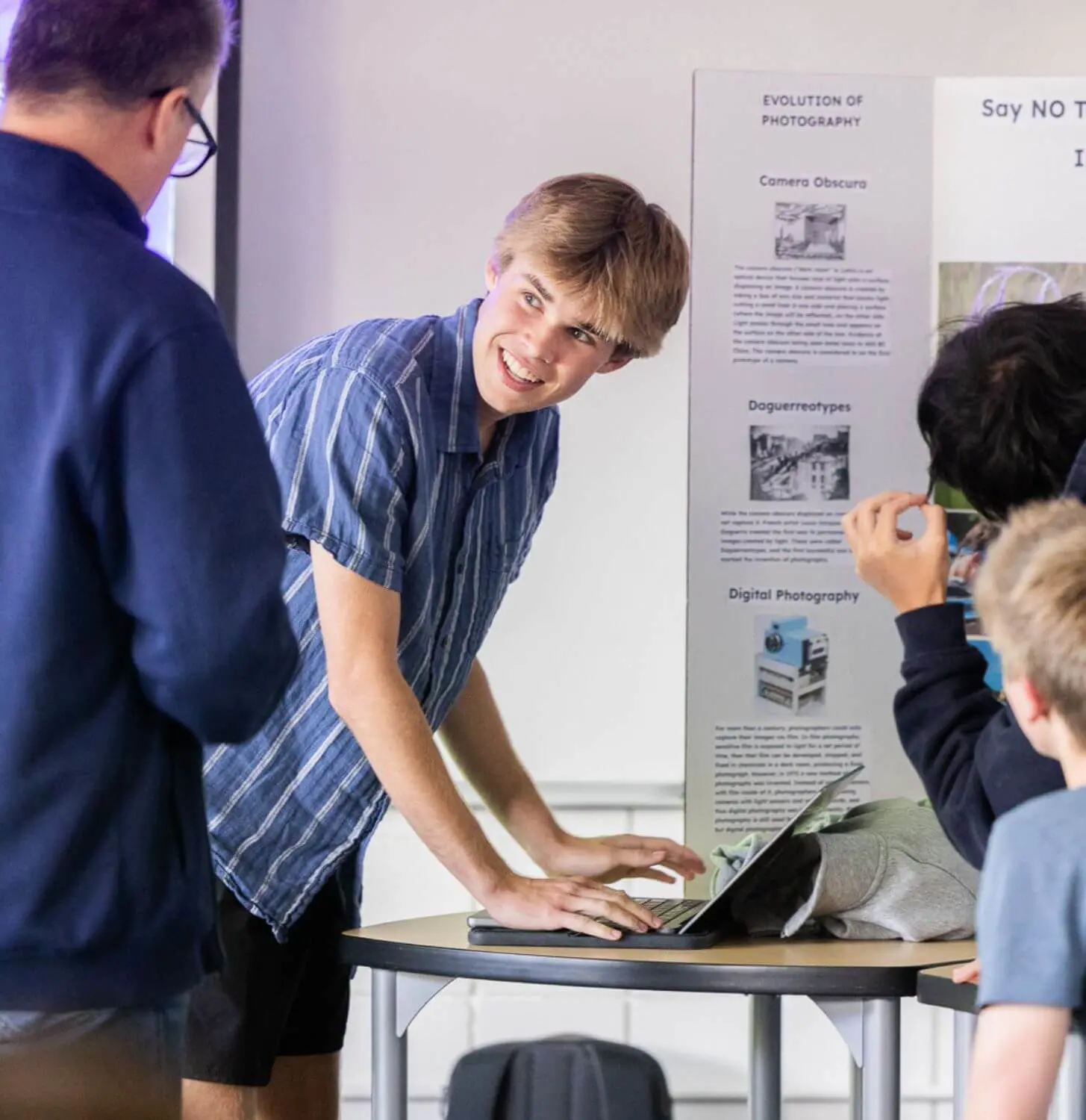 Student working on a laptop looks at their teacher with a smile during class.