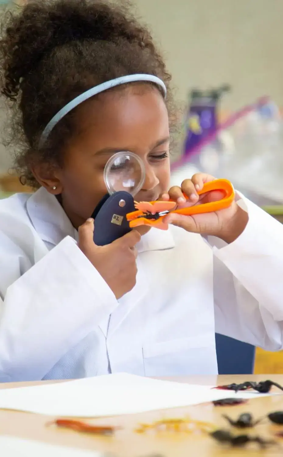 Village student-scientist uses a magnifying glass to observe toy bugs.